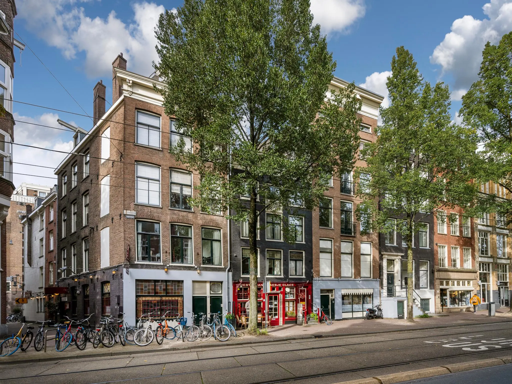 Rij historische panden met winkels en geparkeerde fietsen aan de Nieuwezijds Voorburgwal in Amsterdam.